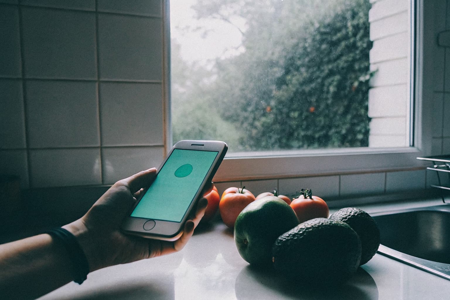 Mano sosteniendo teléfono con app Acopio junto a frutas frescas en cocina